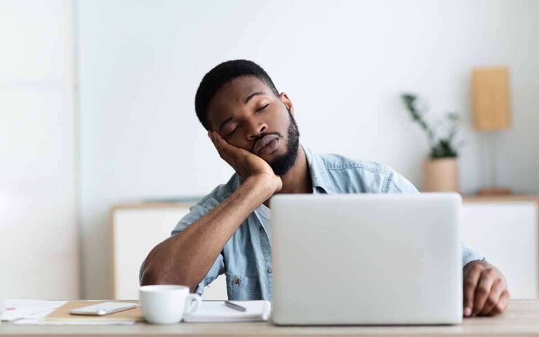 Young man falling asleep at his office desk