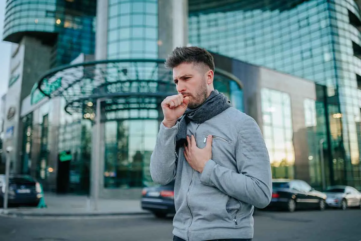 man coughing outside a glass building